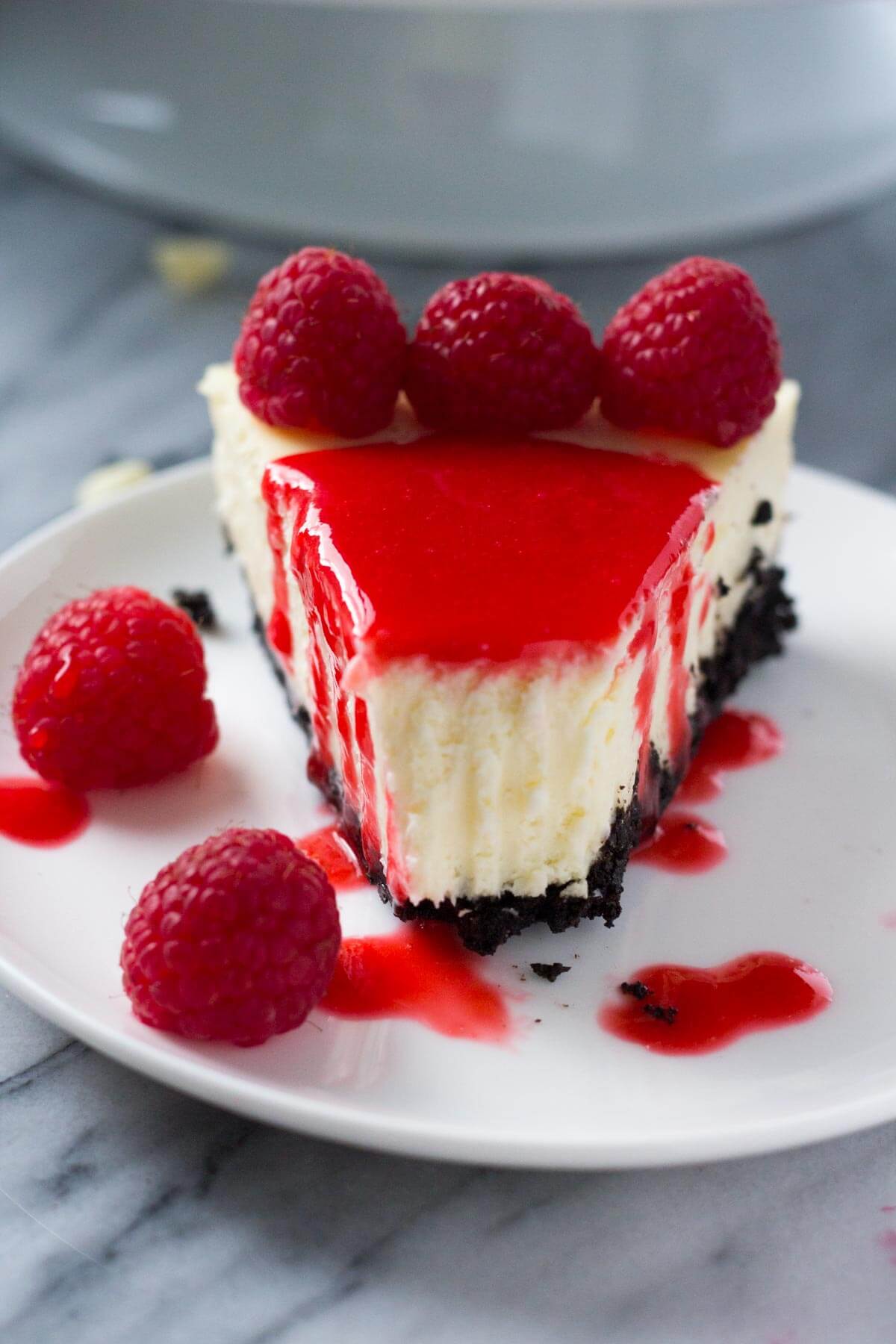 Smooth, creamy White Chocolate Cheesecake with an Oreo cookie crust and Raspberry Coulis Sauce. With easy step by step instructions - it's the PERFECT cheesecake every time!