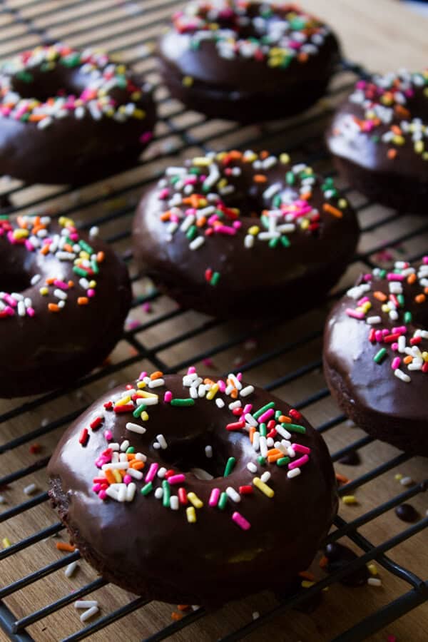 Homemade double chocolate doughnuts with chocolate glaze and sprinkles on a wire cooling rack. 