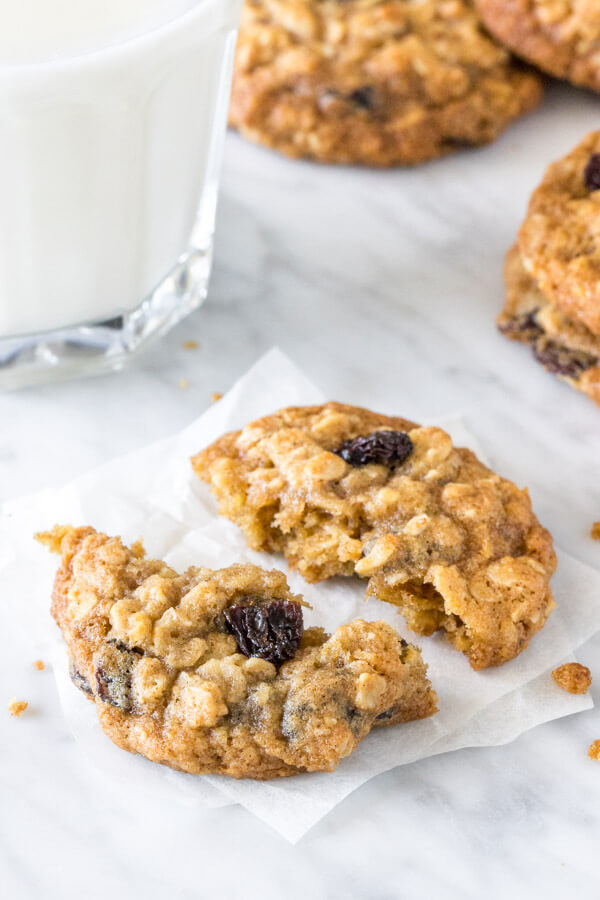 A thick, chewy oatmeal raisin cookie broken in half with a glass of milk.