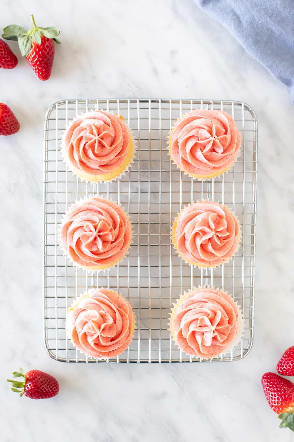 6 cupcakes with pink frosting on a wire cooling rack rack