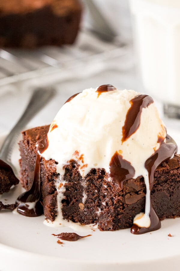 Fudge brownie with a scoop of ice cream and chocolate sauce on top with a bite taken out of it. 