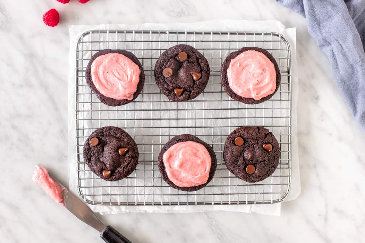 6 chocolate cookies with pink frosting on a wire rack.