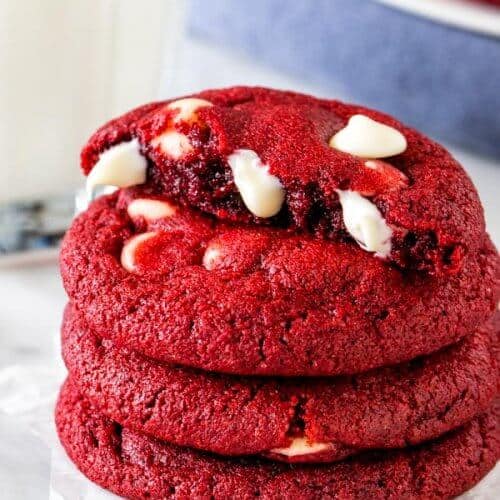 A stack of red velvet chocolate chip cookies, with the top cookie broken in half.