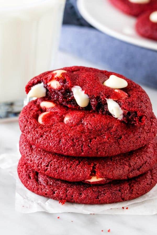 A stack of red velvet chocolate chip cookies, with the top cookie broken in half.