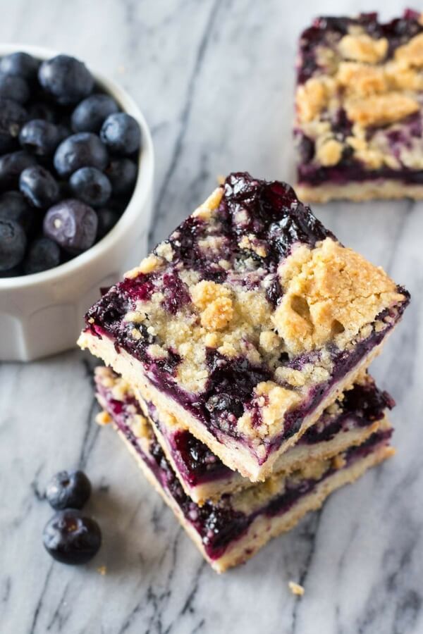 Overhead shot of 3 blueberry crumble bars stacked. A small bowl of fresh blueberries and another bar in the background. 
