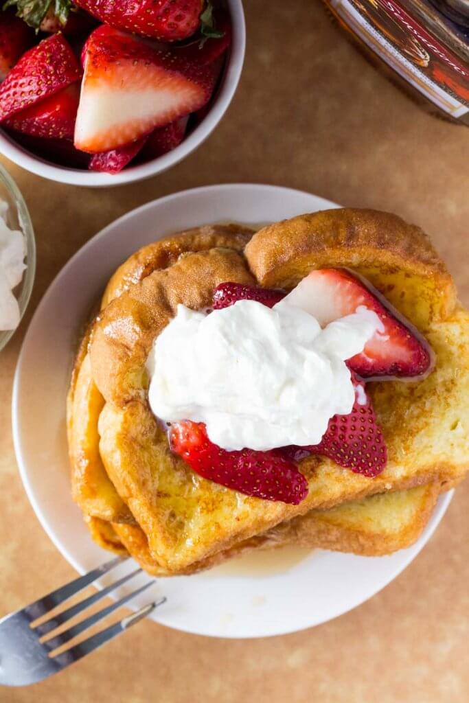 Overhead shot of a stack of french toast with a bowl of strawberries and bottle of maple syrup. 