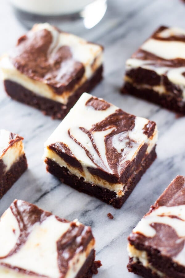 Cream cheese brownies with swirled cheesecake layer on top cut into squares on a marble background. 
