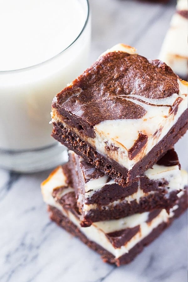 A stack of 3 cream cheese brownies with a glass of milk. 