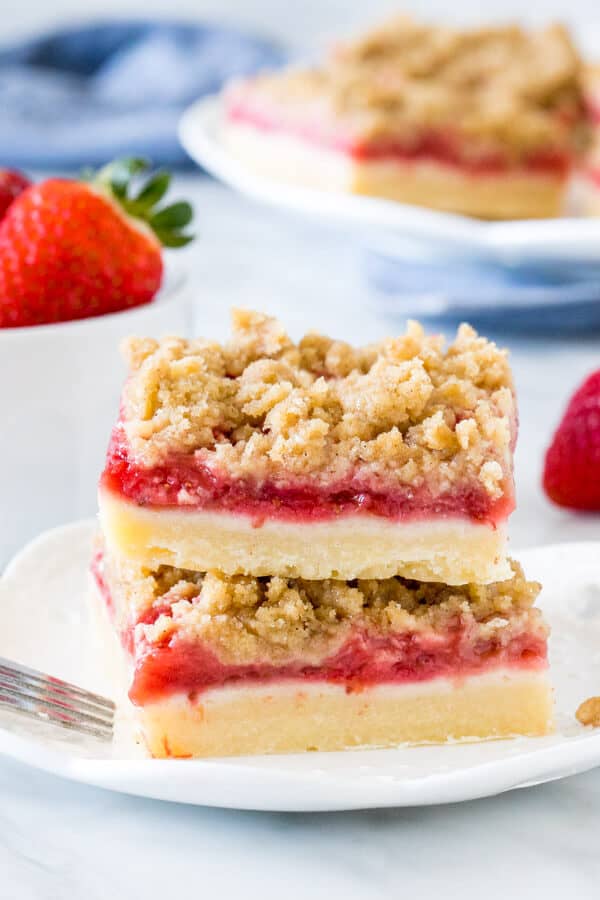 Stack of 2 strawberry crumb bars on white plate with bowl of strawberries.