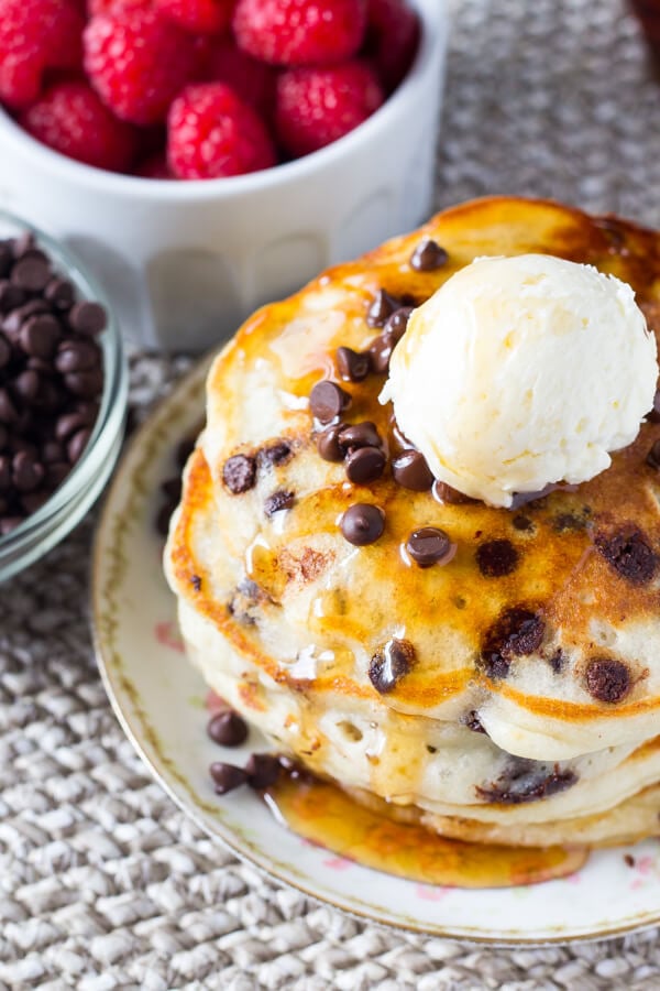 Overhead shot of a stack of fluffy chocolate chip pancakes topped with syrup, chocolate chips, and whipped butter. 