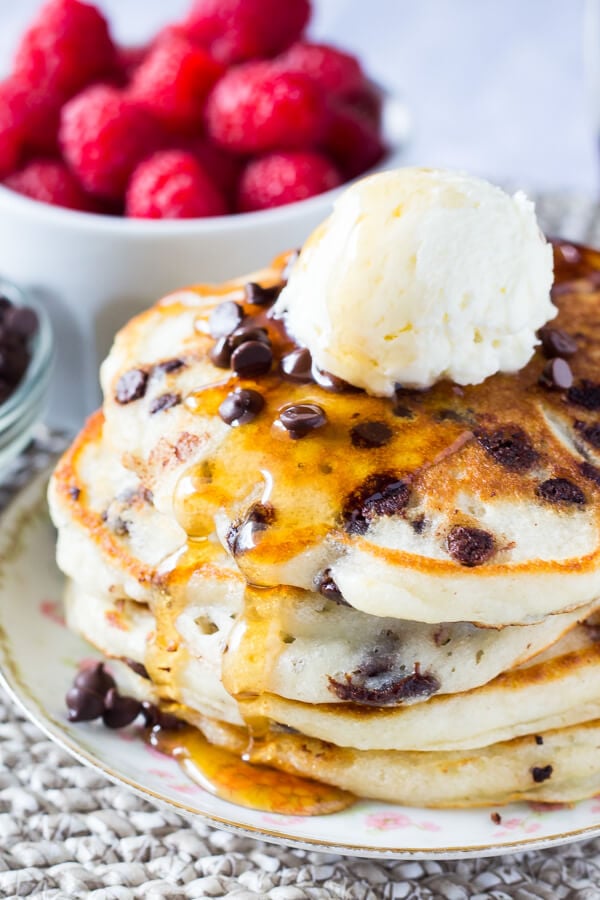 A stack of fluffy buttermilk chocolate chip pancakes drenched in syrup and topped with whipped butter. 