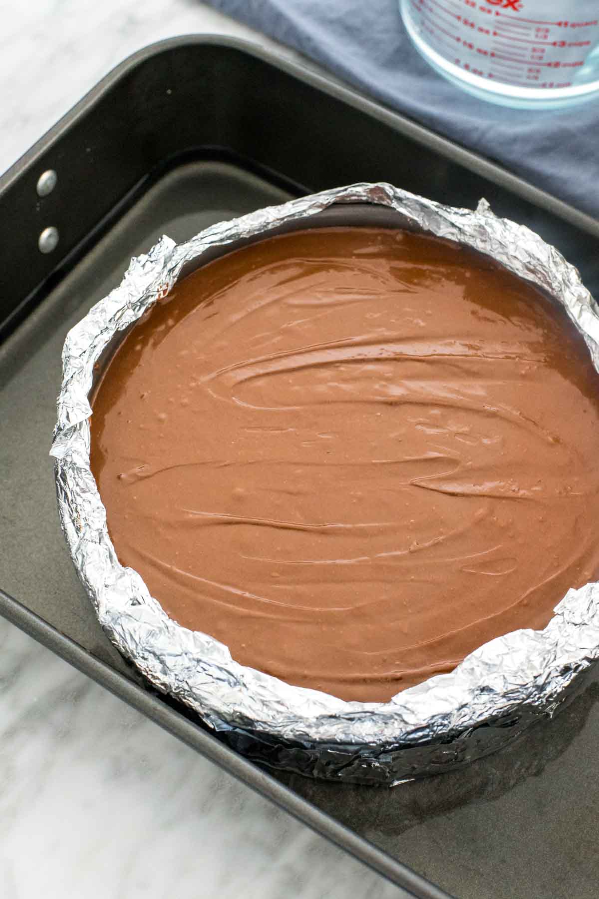 Unbaked cheesecake in a waterbath. Spring form pan wrapped in aluminum foil and placed in the middle of a large roasting pan. 