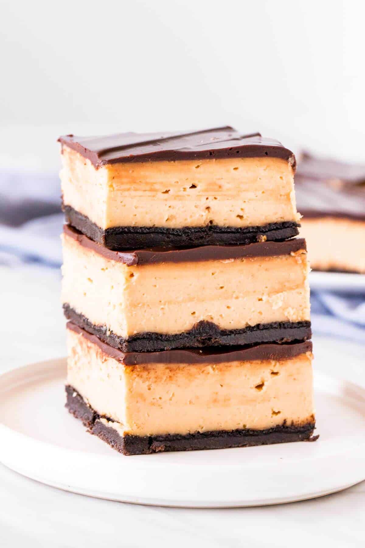Stack of 3 peanut butter cheesecake bars with Oreo crust and chocolate topping.