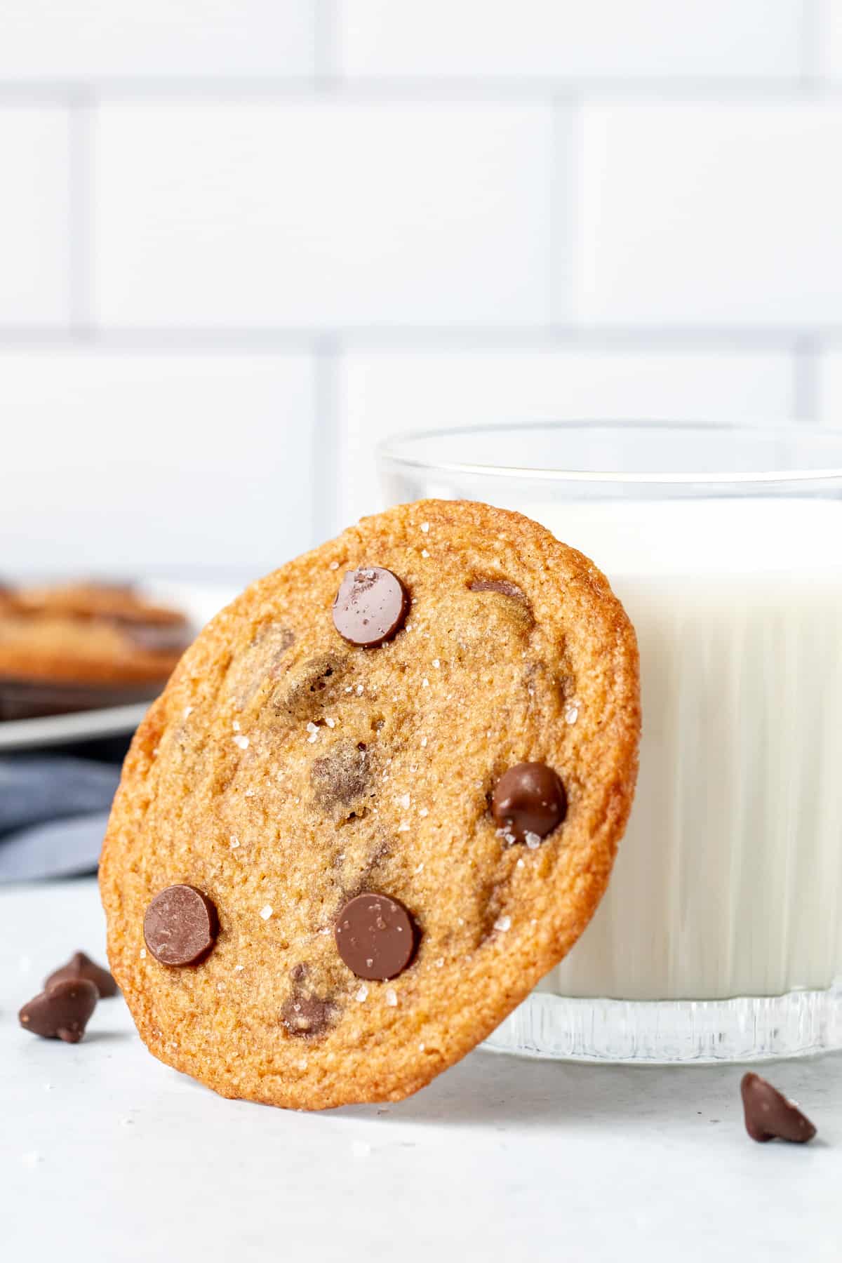 Crispy chocolate chip cookie leaning up against a glass of milk