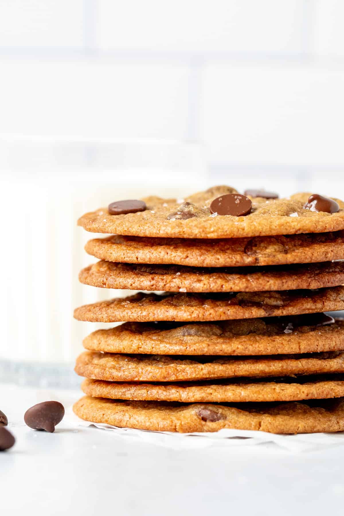 Stack of thin and crispy chocolate chip cookies with glass of milk