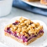 Slice of blueberry oatmeal crumble bar on a plate with bowl of berries.