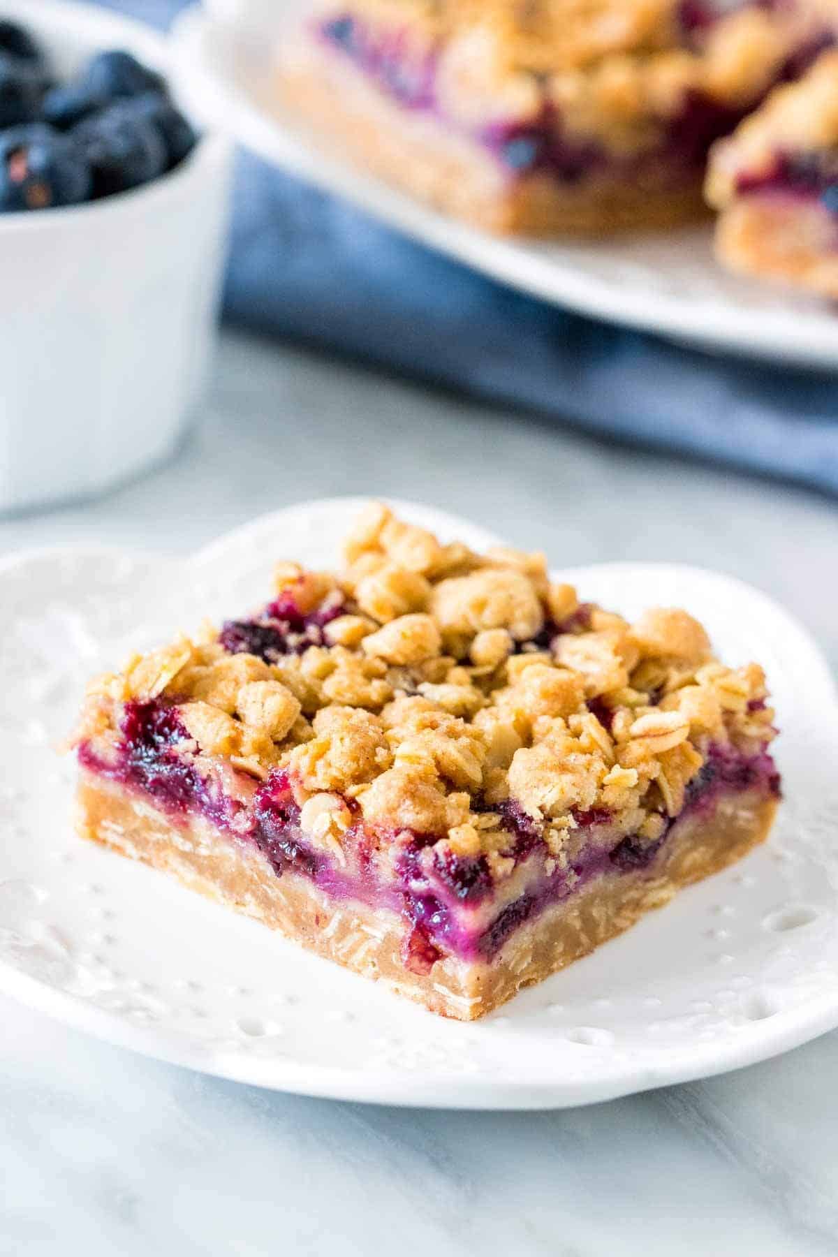 Slice of blueberry oatmeal crumble bar on a plate with bowl of berries. 