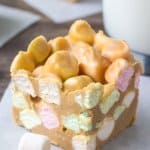 Confetti square made with rainbow marshmallows, butterscotch chips & peanut butter with a glass of milk and 2 squares in the background