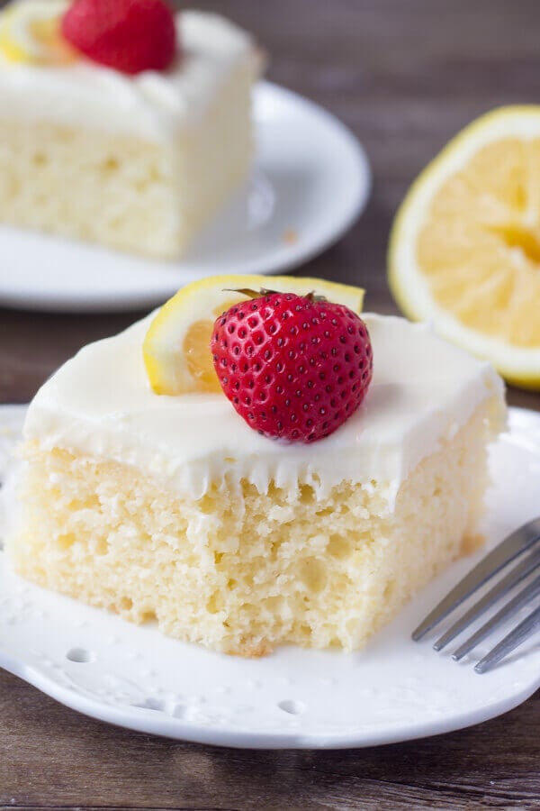 A slice of lemon cake with cream cheese icing with a bite taken out. 
