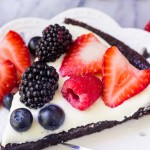 Slice of fruit brownie pizza on a whit plate with fresh berries.
