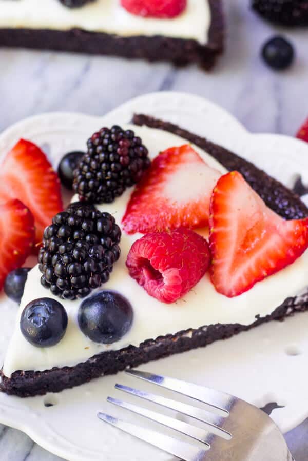 Slice of fruit brownie pizza on a whit plate with fresh berries. 