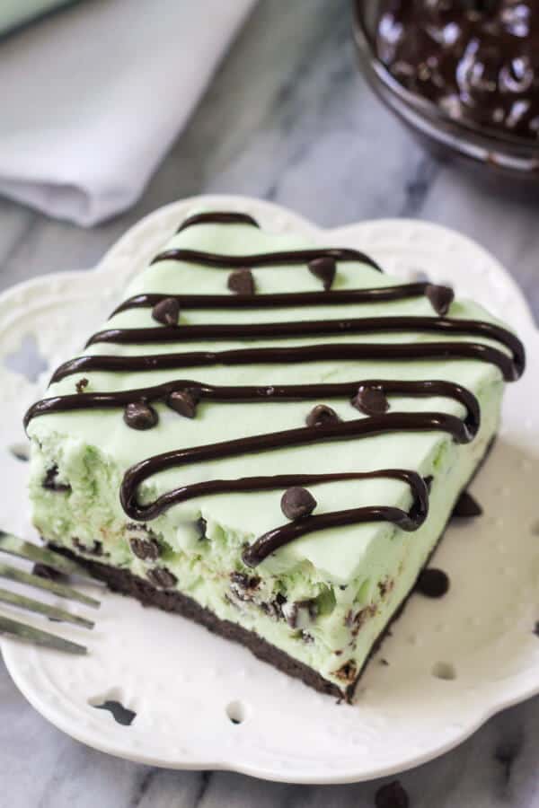 Overhead side angle shot of a slice of mint chip ice cream cake drizzled with fudge sauce. White napkin in the background
