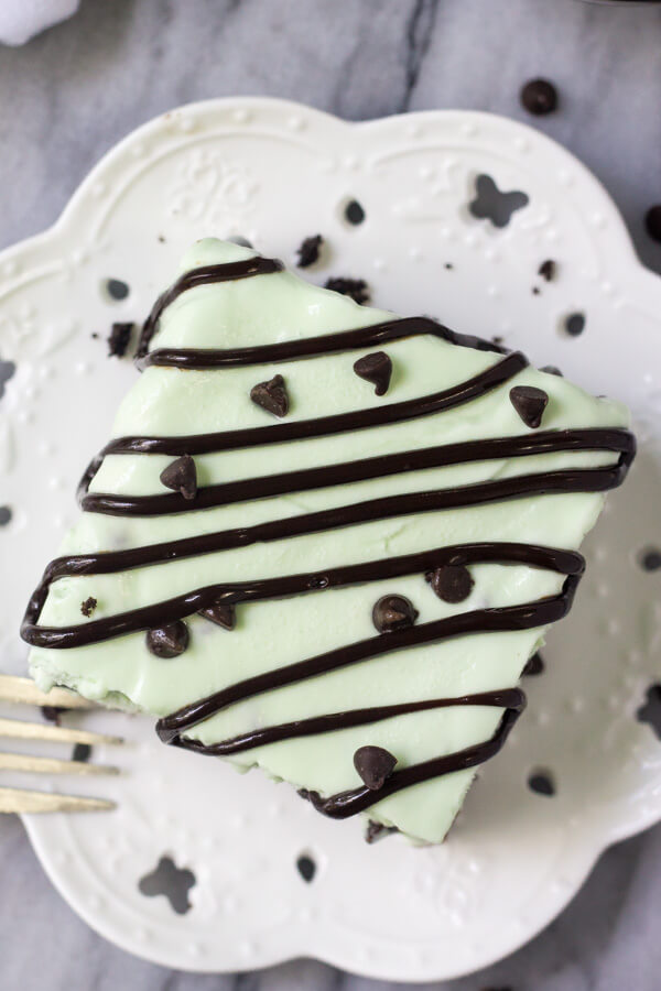 Overhead shot of a square slice of mint chip ice cream cake drizzled with chocolate sauce on a white plate
