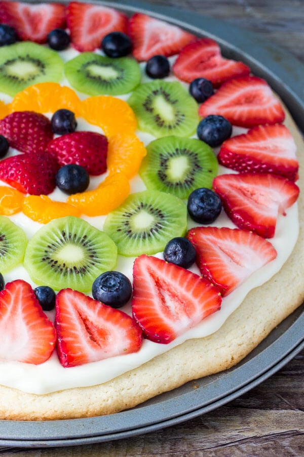 Whole sugar cookie fruit pizza topped with strawberries, blueberries, kiwis and mandarin oranges in it's pizza pan. 