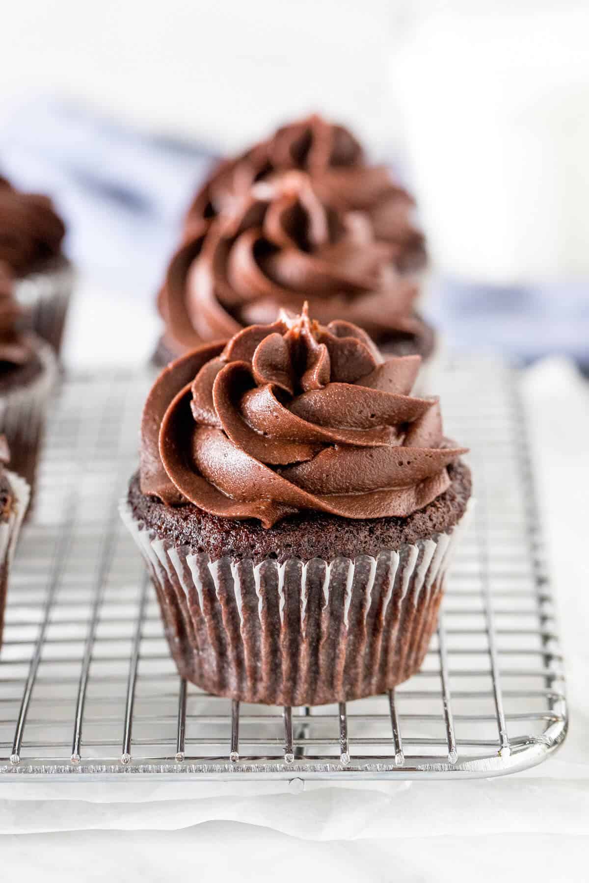 Chocolate cupcakes with chocolate frosting on cooling rack.
