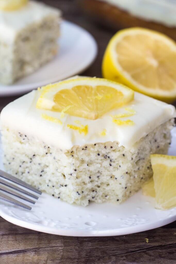 Slice of lemon poppy seed cake with cream cheese frosting with a bite taken out of it. Garnished with lemon slices. 