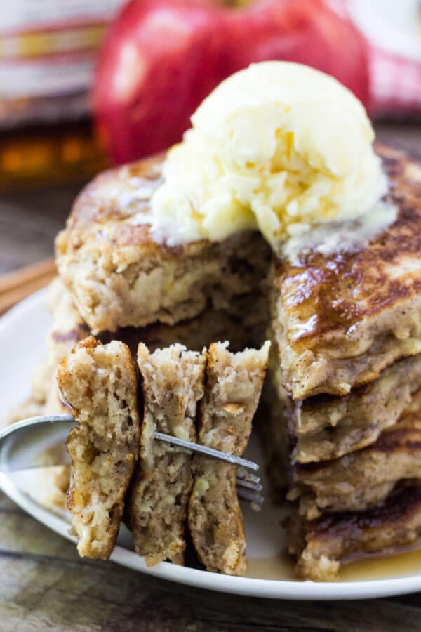 Bite of apple pancakes on a fork with stack of pancakes in the background