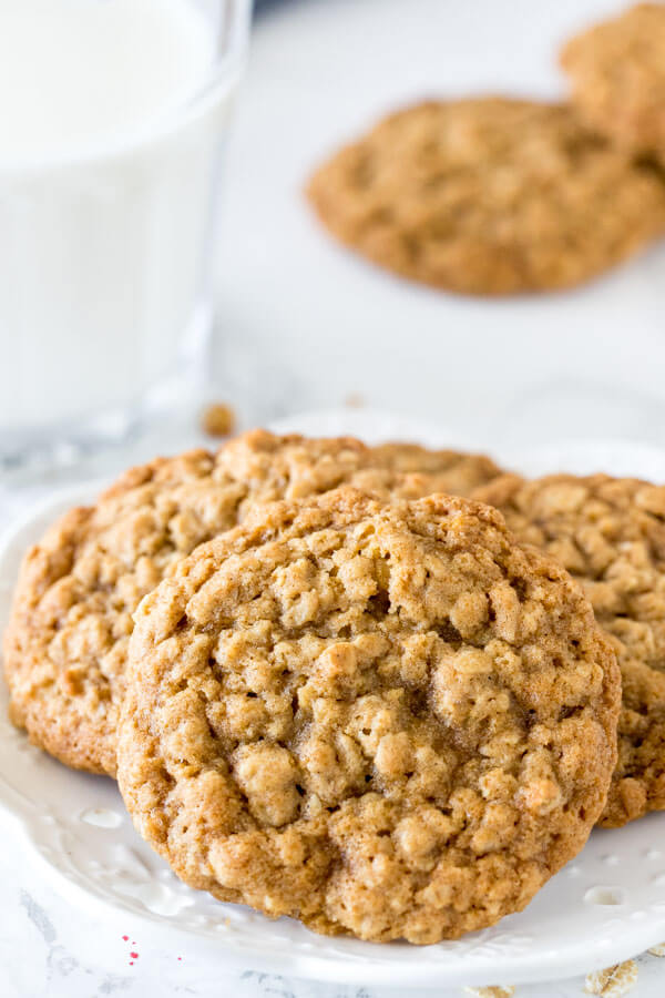 A plate of 3 oatmeal cookies with a glass of milk. 