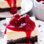 A slice of brownie cheesecake bars topped with cherry pie filling. They have a fudgy brownie bottom and a layer of creamy cheesecake on top.