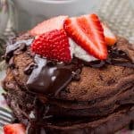 A stack of fluffy chocolate pancakes with chocolate ganache, strawberries and whipped cream is the ultimate breakfast for chocolate lovers.
