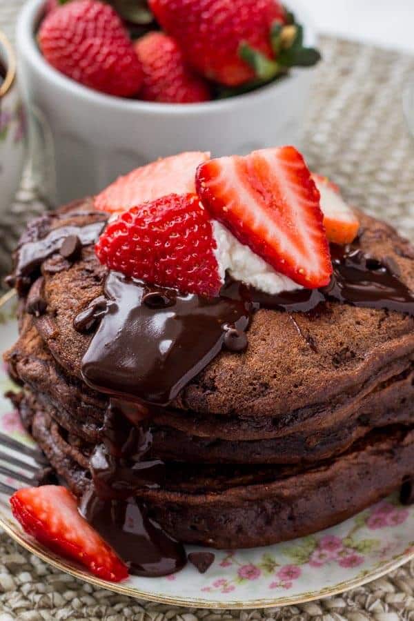 A stack of fluffy chocolate pancakes with chocolate ganache, strawberries and whipped cream is the ultimate breakfast for chocolate lovers. 