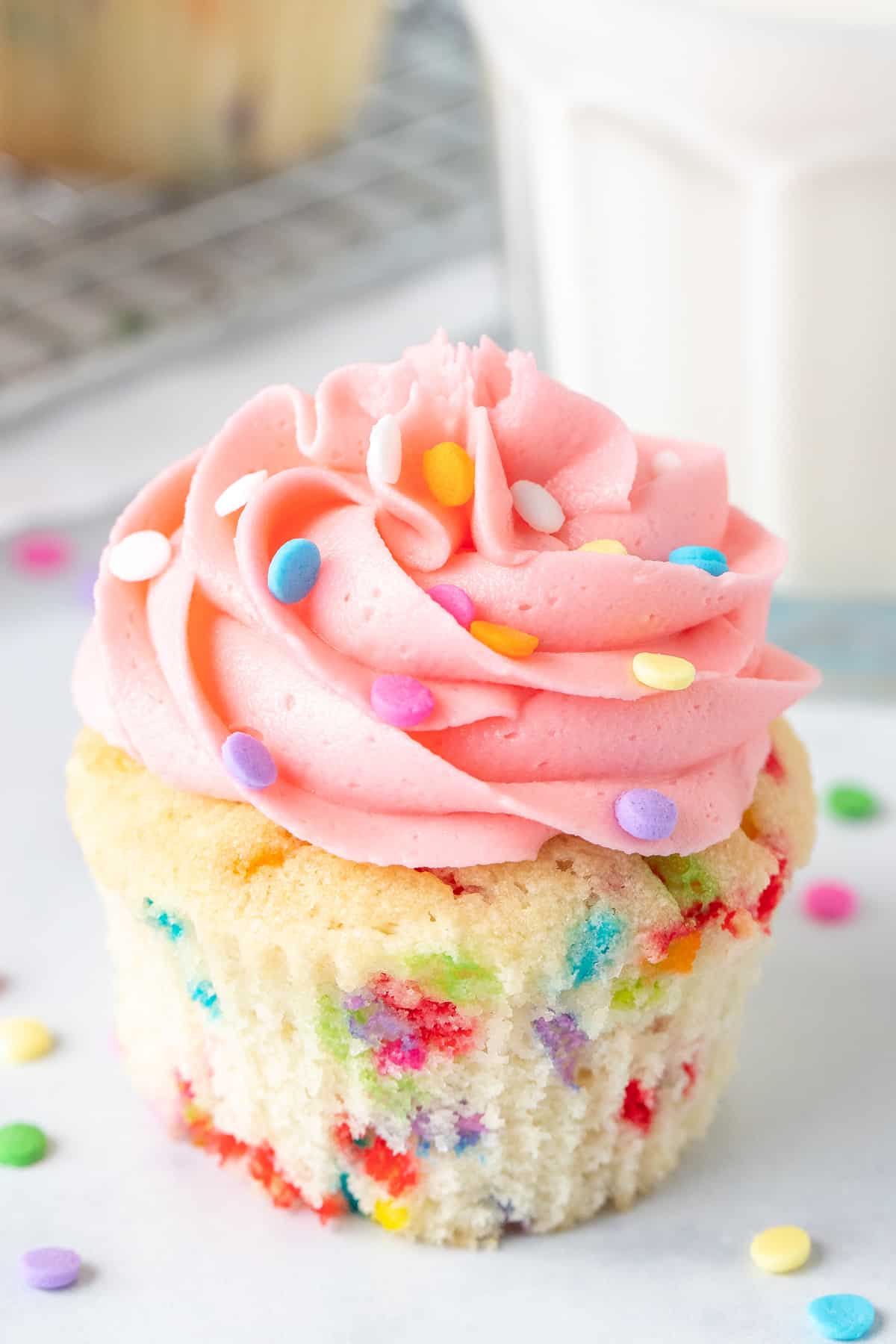 Funfetti cupcake with pink frosting and glass of milk