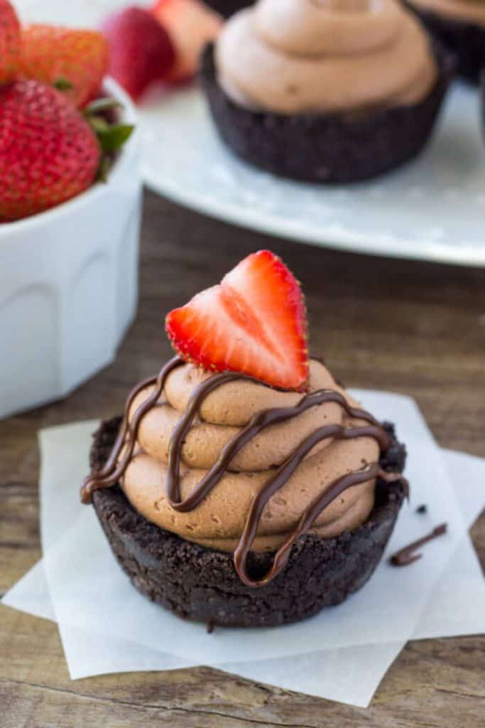 Mini no bake chocolate cheesecakes with an Oreo crust, drizzle of chocolate and topped with a strawberry. 