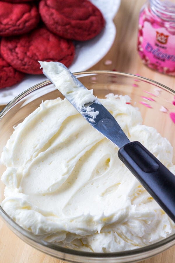 A bowl of fluffy cream cheese buttercream ready for frosting on red velvet cookies. 