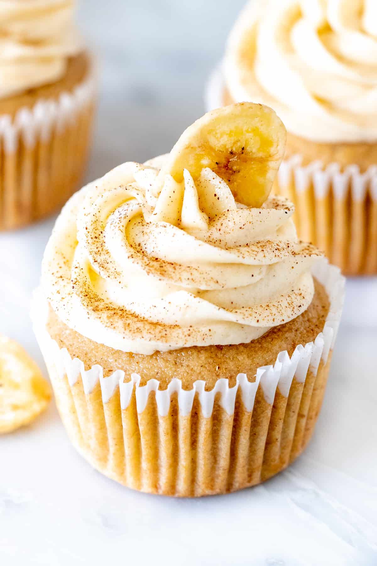 Banana cupcake frosted with cinnamon cream cheese frosting and topped with a banana chip