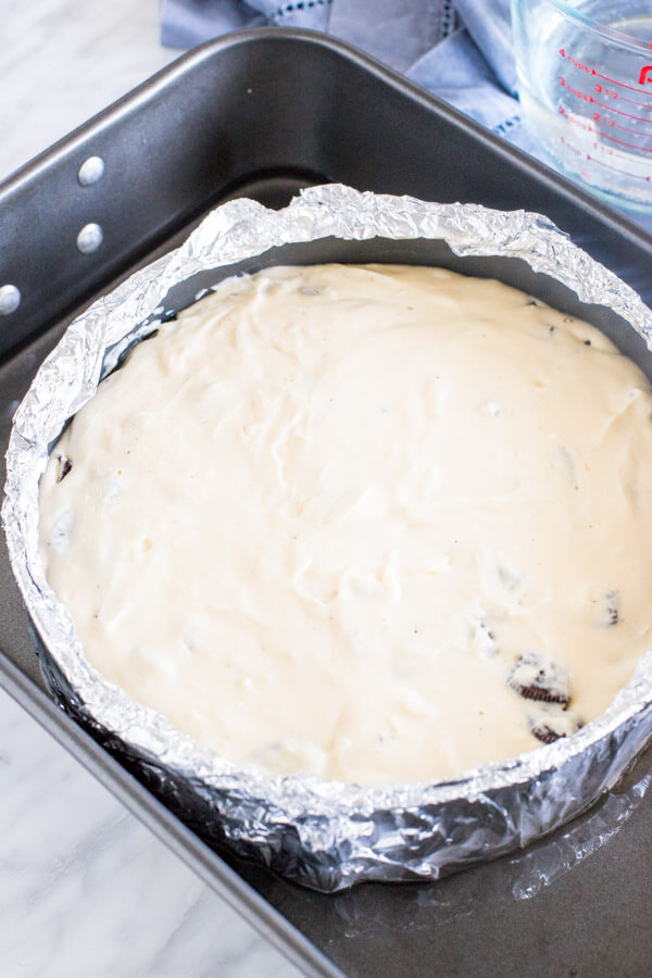 Unbaked oreo cheesecake in a water bath with the spring form pan wrapped in aluminum foil and placed inside a large roasting pan with water. 