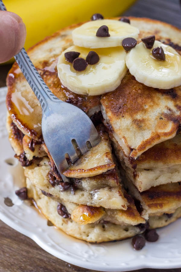 A stack of  extra fluffy banana chocolate chip pancakes drizzled with syrup