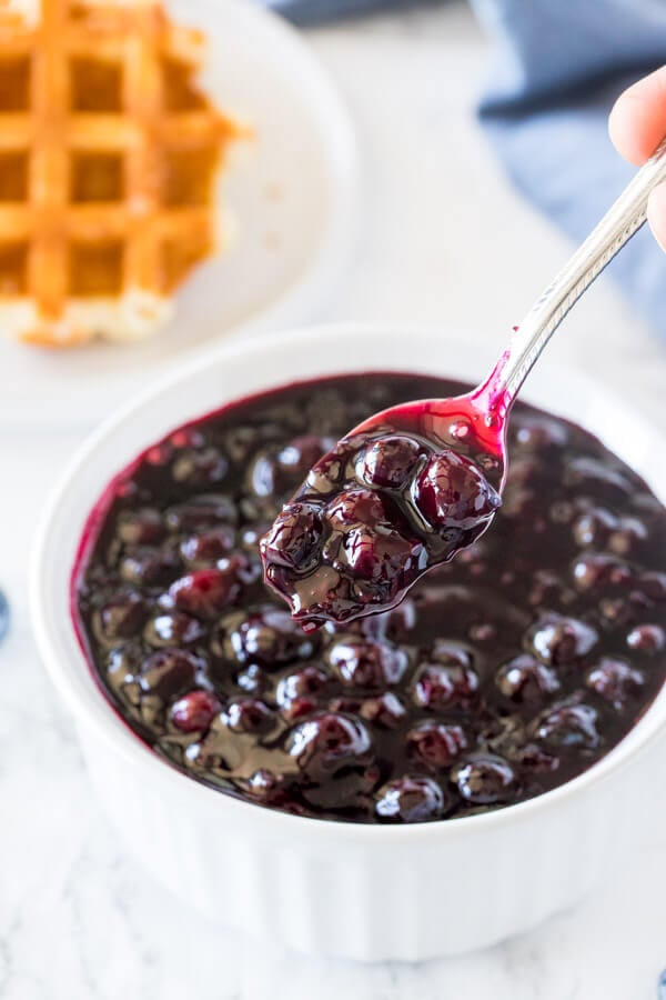 A bowl of homemade blueberry sauce with a spoon taking some out of the bowl.