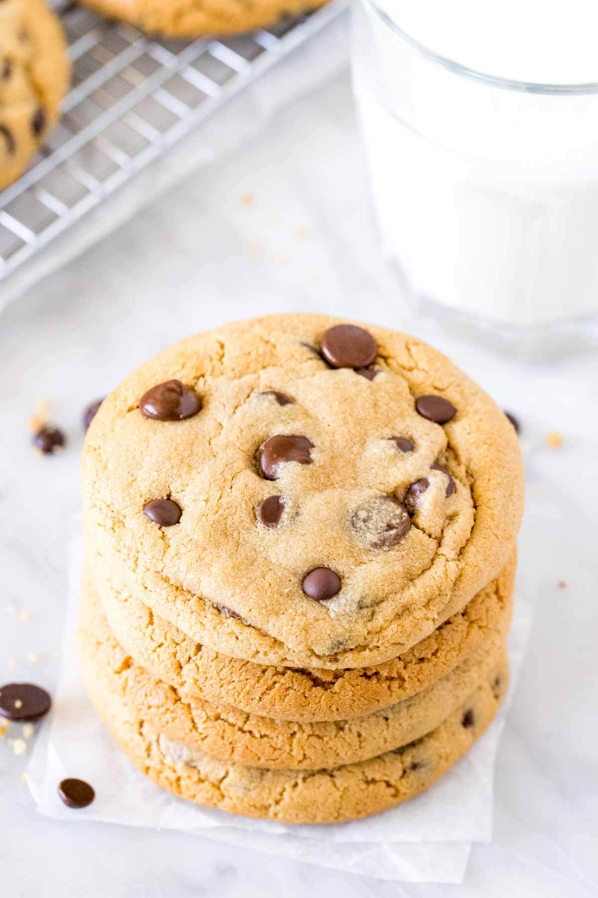 Stack of chewy peanut butter cookies filled with chocolate chips with a glass of milk. 