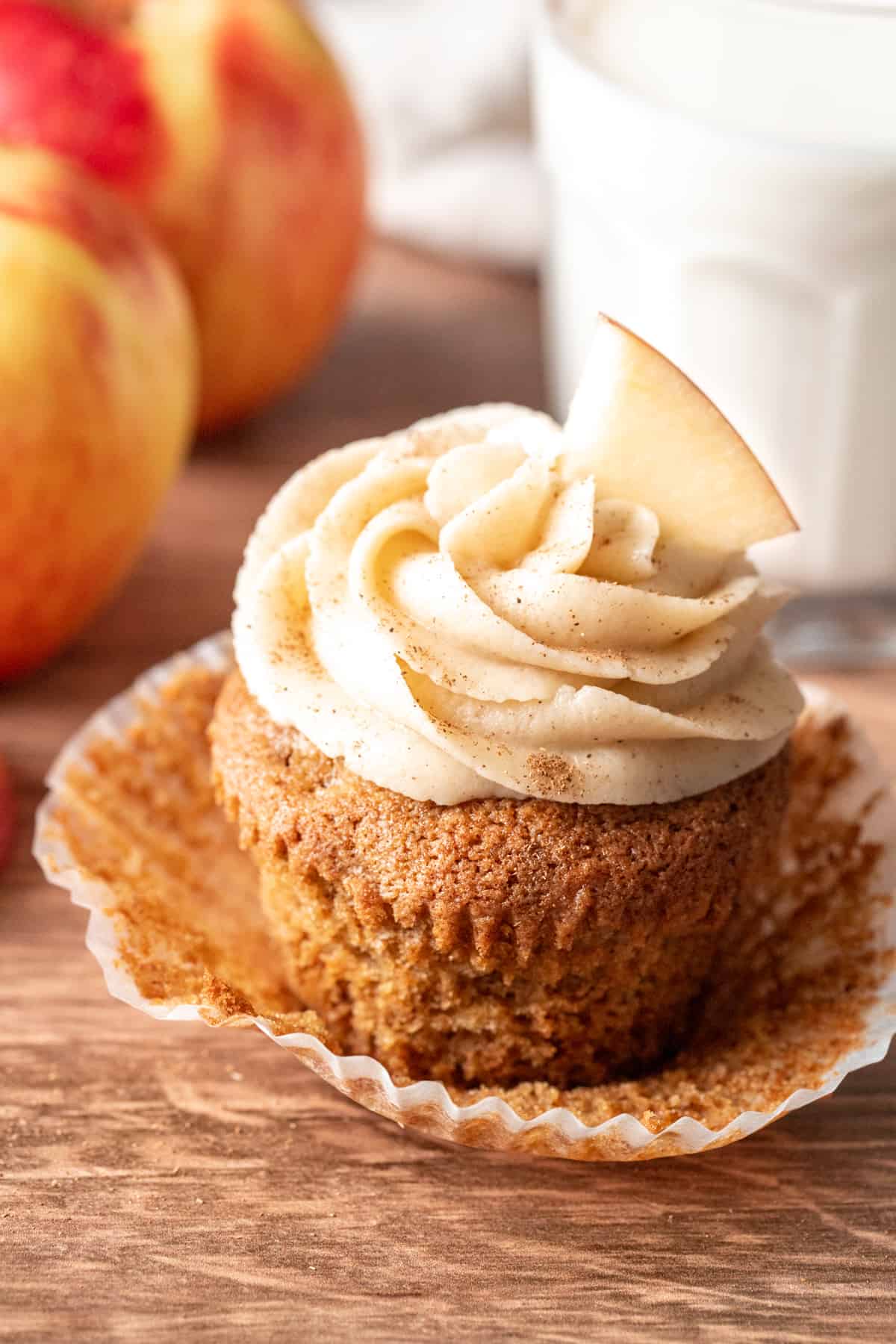 Apple cupcake with cream cheese frosting topped with slice of apple and a glass of milk