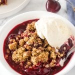 A bowl of cherry crisp with brown sugar oatmeal topping and a scoop of vanilla ice cream.