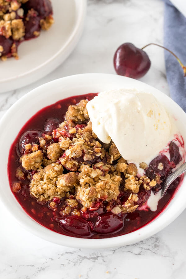 A bowl of cherry crisp with brown sugar oatmeal topping and a scoop of vanilla ice cream.