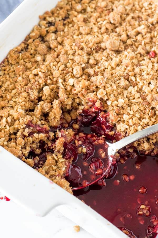 A 9x13 inch pan of cherry crisp fresh from the oven, with a close up on the serving spoon with juicy cherries. 