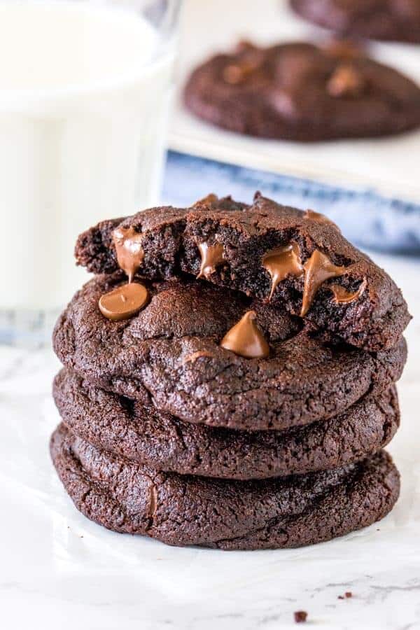 A stack of thick double chocolate chip cookies with the top cookie broken in half. 