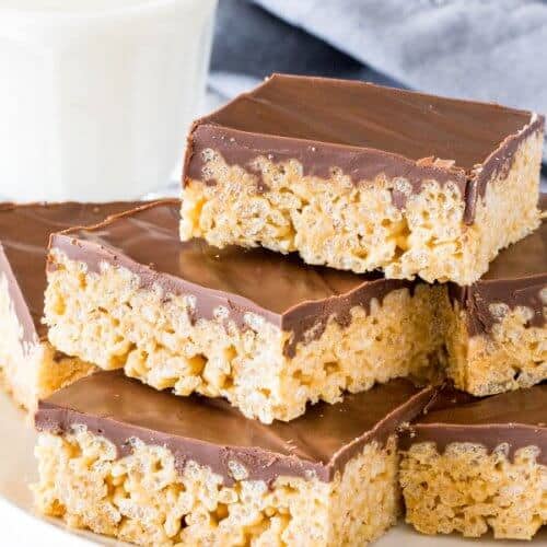 A plate of peanut butter chocolate rice krispie treats stacked on top of eachother with a glass of milk.