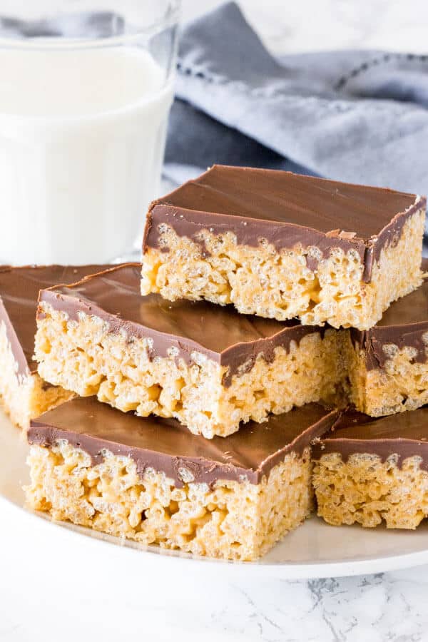 A plate of peanut butter chocolate rice krispie treats stacked on top of eachother with a glass of milk. 